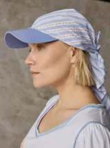 Gorro tipo gorra con visera rígida celeste y pañuelo integrado de tela a rayas blancas y celestes, con detalles de bordado a mano en color naranja.