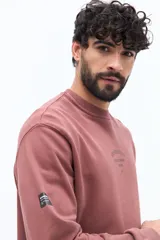 Buzo de algodón color rosado oscuro o terracota, con cuello redondo y puños acanalados. Presenta un pequeño logo estampado en el pecho con el texto "BROOKSFIELD COVENT GARDEN LONDRES".