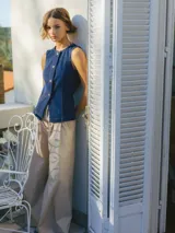 Chaleco de denim azul con escote en V, botones dorados y ribete de cuentas en el cuello.