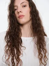 Remera de manga larga entallada confeccionada en tejido pointelle suave, con escote a la base y detalle de pequeño lazo decorativo en el centro. Presenta terminaciones con borde picot.