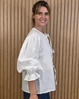 Camisa color beige de lino con mangas abullonadas tres cuartos y cierre frontal mediante múltiples lazos para atar.