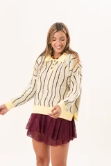 Buzo de punto tipo polo en tono amarillo claro con diseño de ondas a rayas en tonos marrón y celeste. Presenta cuello clásico, cierre frontal parcial con botones y silueta relajada con mangas largas.