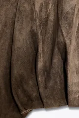 Chaqueta bomber de efecto ante en color marrón, con cuello solapa, manga larga y trabillas en los hombros. Presenta un diseño con volumen en el bajo acabado en pliegues y cierre frontal con botones ocultos.