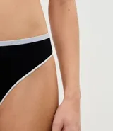 Bombacha tipo bikini de corte tanga, confeccionada en poliamida con elastano. Presenta un diseño sin costuras en color negro con bies contrastante en tono claro en los bordes.