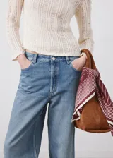 Jeans de tiro medio en denim azul con lavado medio, corte recto y amplio, diseño clásico de cinco bolsillos y cierre frontal con botón y cremallera.