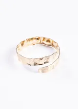 Brazalete dorado abierto, con textura martillada y diseño entrelazado.