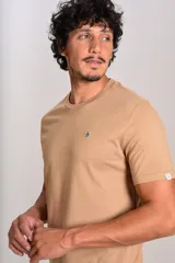 Remera de manga corta con cuello redondo, confeccionada en algodón de color beige. Presenta un pequeño logo bordado de un pingüino en el pecho.