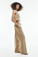 Pantalón de tiro medio color beige con sutiles rayas verticales blancas, de corte recto y amplio. Cuenta con bolsillos delanteros y un cinturón trenzado del mismo tejido con cordón ajustable.