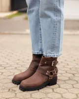 Botas cortas de cuero color caoba, con suela track negra, cierre lateral y correas con hebillas metálicas decorativas.