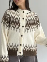 Cardigan de punto con diseño jacquard de inspiración nórdica, en tonos blanco, gris y marrón. Presenta cuello redondo, cierre frontal con botones y mangas largas con puños acanalados.