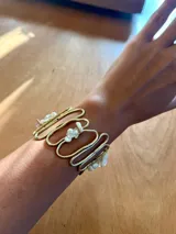 Pulsera dorada con diseño de líneas onduladas y apliques de piedras blancas.