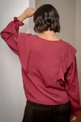 Blusa blanca de algodón con cuello redondo, mangas largas con puños elásticos y volados decorativos en los hombros.