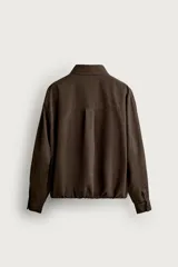 Cazadora de corte relajado color marrón, confeccionada en tejido de algodón. Presenta cuello solapa, cierre frontal con botones, bolsillo plastrón en el pecho, bolsillos laterales de vivo y bajo ajustable con elástico en los laterales.