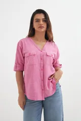 Camisa de manga tres cuartos con puños enrollados, escote en V y botones frontales. Presenta dos bolsillos de parche con solapa y botón en el pecho. El tejido es de color rosa jaspeado.