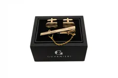 Set de gemelos y sujetacorbata dorados con diseño geométrico, presentados en caja negra de la marca Guarnieri.
