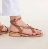 Sandalias de cuero color marrón con tiras cruzadas y tobillera con hebilla.