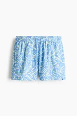 Short de baño celeste con estampado tropical en tonos claros, cintura elástica con cordón de ajuste y bolsillos laterales.