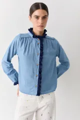 Camisa de jean azul claro con detalles de crochet en color azul oscuro en el cuello, la botonera frontal y los puños. Presenta un corte recto, mangas largas y botones de madera.