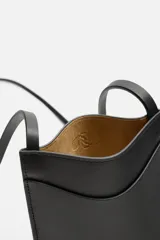 Bolso bandolera negro de cuero con bolsillo plano frontal y correa larga del mismo material.