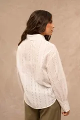 Camisa blanca de manga larga con diseño bordado y calado en patrón de rayas verticales. Posee cuello clásico, cierre frontal con botones y puños anchos.