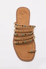 Sandalia plana negra con tiras finas decoradas con tachas y piedras turquesas, con diseño de sujeción para el dedo y puntera cuadrada.
