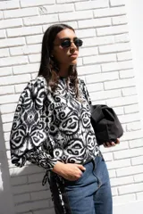 Blusa estampada en blanco y negro, con cuello redondo y mangas globo de puños elastizados largos. Presenta tiras ajustables en los laterales.