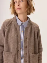 Saco de lana color marrón, de tejido grueso, con cuello redondo y botones frontales. Presenta mangas raglán con detalle de punto acanalado y bolsillos delanteros tipo parche.