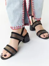 Sandalias de tacón redondo de 6 cm, con diseño de tiras en gamuza negra y bandas frontales translúcidas de TPU. Incluye cierre con pulsera fina al tobillo.