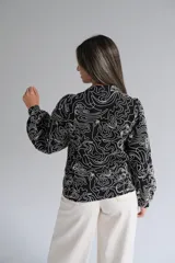 Blusa de manga larga con cuello mao y cierre frontal de botones. Presenta un diseño estampado con líneas blancas abstractas sobre fondo negro.