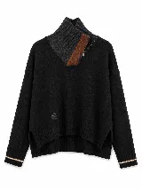 Polera tejida en lana lambswool, de color negro con cuello alto y cierre frontal parcial. Presenta un diseño de rombos en relieve en las mangas y detalles de rayas en contraste en los puños. El diseño incluye un dobladillo asimétrico con aberturas laterales.