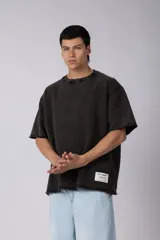 Remeron de corte oversized con cuello redondo y mangas cortas. Presenta un acabado de tela con efecto desgastado y costuras visibles en los bordes, con una etiqueta pequeña en el lateral inferior.