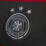 Camiseta de fútbol Adidas de la selección de Alemania, modelo visitante (Away) de 2014. Diseño de rayas horizontales anchas en color negro y rojo, con cuello mao abotonado y detalles de las franjas de Adidas en los hombros.
