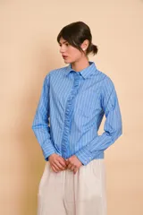Camisa de manga larga color celeste con rayas verticales blancas, cuello camisero y volados frontales a lo largo de la botonera.