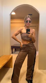 Pantalón marrón de gamuza con flecos laterales y ajuste con cordones en la cintura.