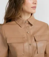 Camisa de manga corta confeccionada en cuero sintético color tostado, con cuello camisero, cierre frontal con botones en forma de corazón y dos bolsillos con solapa en el pecho.