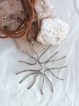 Colgante plateado con dije abstracto en forma de coral y cordón de cuero marrón.