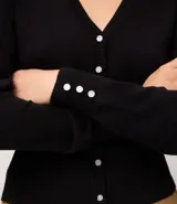 Cardigan negro de punto con cuello en V, mangas largas y cierre frontal con botones perlados.