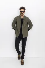 Camisa verde militar de corte recto, con cuello clásico, cierre frontal con botones a presión, mangas largas con puños abotonados, dos bolsillos de parche en el pecho y bajo redondeado.