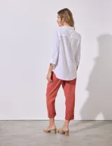 Camisa blanca de corte clásico con textura de líneas verticales, cuello con solapa, cierre frontal con botones y bolsillo en el pecho. Presenta mangas tres cuartos regulables con presilla y botón.