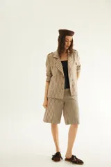 Chaqueta corta de inspiración motoquera color beige, confeccionada en lino fantasía, sin forro, con cierres decorativos, broches de presión y bolsillos delanteros funcionales. Presenta detalle bajo el cuello y en vueltas de mangas en color mostaza y rayas.