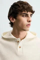 Sudadera de corte relajado confeccionada en tejido de algodón con textura waffle. Presenta cuello con capucha, cierre frontal parcial con botones y mangas largas con puños acanalados.