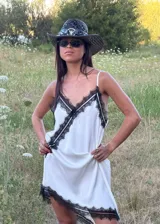 Vestido corto tipo lencero de seda color blanco, con detalles de encaje negro en el escote en V y en el ruedo asimétrico. Presenta breteles finos ajustables y una caída fluida.