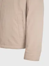 Campera Tommy Hilfiger color beige con cierre de cremallera, cuello doblado y dos bolsillos laterales. Tiene detalles distintivos de la marca y el logo bordado en el pecho.