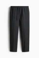 Pantalón tipo jogger de vestir con pliegues frontales y traseros, cintura elástica con cordón de ajuste, bolsillos laterales al bies y bolsillos traseros insertados. Presenta un corte slim fit entallado.