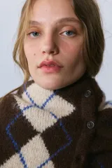 Chaleco de punto con cuello redondo y diseño sin mangas. Presenta un patrón de rombos en tonos marrón y beige con detalles en azul.