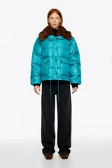 Campera acolchada corta de tejido técnico en color turquesa, con cierre frontal de cremallera y botones de presión. Presenta cuello con detalle de pelo sintético desmontable, bolsillos frontales con tapeta y bolsillo con cierre en la manga.