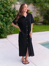 Vestido camisero de muselina color negro, de largo midi, con cuello clásico, manga corta y cierre frontal con botones.