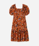 Vestido corto color ladrillo con estampado de flores y palmeras en tonos blanco y negro. Tiene escote cuadrado, mangas cortas abullonadas y falda con volantes.