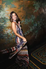Vestido largo de encaje y transparencias color marrón, con escote profundo halter, frunces en el cuerpo, espalda abierta y tiras largas estampadas para atar al cuello.