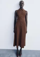 Vestido midi marrón sin mangas, de corte evasé y diseño estilo camisero con cuello clásico, cierre frontal con botones y cinturón ajustable con hebilla.